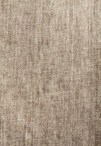 Primo piano di tessuto beige intrecciato con un motivo a spina di pesce delicato che crea un effetto testurizzato a strisce diagonali.