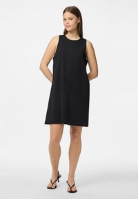 Juoda be rankovių suknelė su apvaliu iškirpimu, švelni tekstūra ir laisvas siluetas, derinama su juodomis plokščiais dirželiais sandalais.