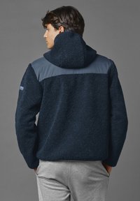 Maritieme fleecejas met een gestructureerd oppervlak, een capuchon en een glad schouderpaneel. Heeft een klein logo op de linkermouw.