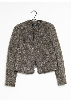 Brun og hvid tekstureret tweed dameblazer med lange ærmer hængende på en sort bøjle mod en hvid baggrund.