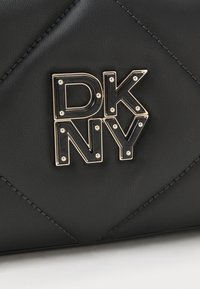 Svart läderhandväska med quiltad design, med en metallisk DKNY-logotypaccent i silver med små nitar. Slät textur, inga ytterligare detaljer.