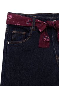 Jeans de mezclilla oscura con un cinturón de lazo de estampado floral burdeos, que cuentan con un bolsillo frontal, costuras doradas y una cinturilla resistente.