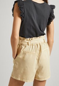 Czarny bawełniany top z falbanami na rękawach z ażurem, połączony z jasnobeżowymi szortami z elastycznym stanem, wyposażonymi w boczne kieszenie oraz kieszenie naszywane z tyłu.