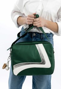 Grøn nylon taske med et hvidt og sølvfarvet geometrisk mønster. Har en bærestrop og en nøglering med baseball-tema.