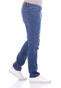 Jeans in denim blu con vestibilità slim, design a cinque tasche e un'etichetta in pelle marrone sulla cintura. Abbinati a sneaker bianche.