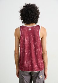 Débardeur sans manches bordeaux avec un motif texturé, un ourlet blanc et un logo au dos, associé à un short cargo gris.