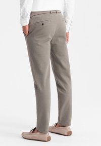 Pantalon gris à coupe droite, deux poches arrière et fermeture à bouton. Le matériau semble lisse avec un léger brillant, associé à des chaussures beiges.