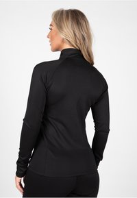 Top negro de manga larga con cuello alto, fabricado en material suave y elástico, que presenta un corte ajustado y sutiles detalles de diseño sin costuras.