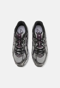 Baskets de sport en mesh noir et gris avec un bout rond, des accents violets et une semelle en caoutchouc texturée, dotées de lacets pour un maintien sécurisé.