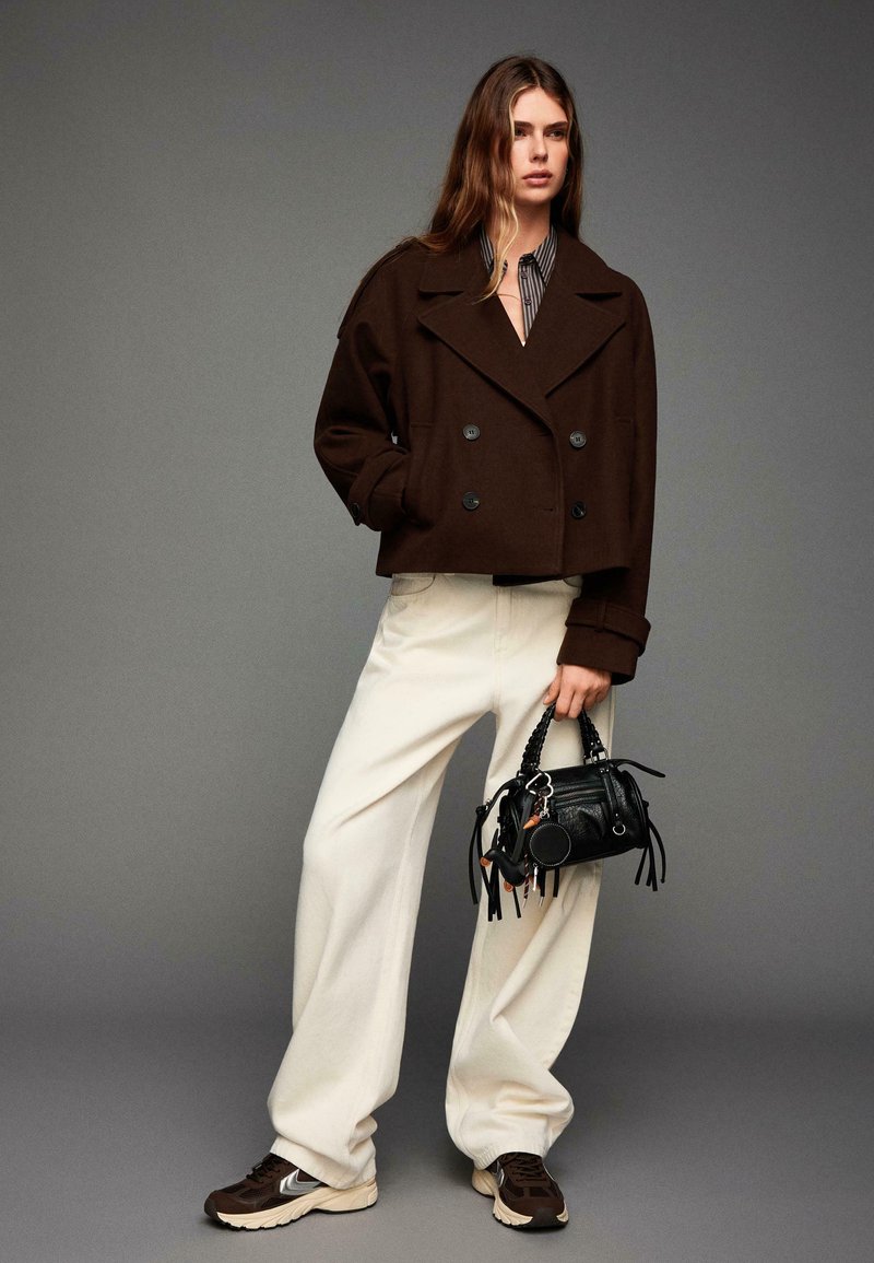 Veste cropped marron à double boutonnage, chemise rayée, pantalon large blanc, baskets marron et petit sac noir avec des franges.