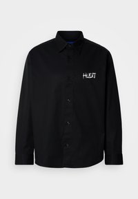 Μαύρο πουκάμισο με κουμπιά από βαμβάκι, με γιακά και μακριά μανίκια. Φέρει λευκό κεντημένο λογότυπο στην αριστερή πλευρά του στήθους.