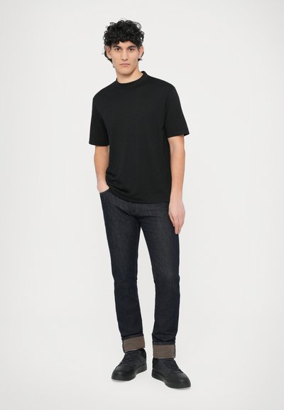 Fekete, rövid ujjú póló laza szabással, sötét farmernadrággal és fekete sportcipővel párosítva. Egyenes szárú farmer, felhajtott szegéllyel.