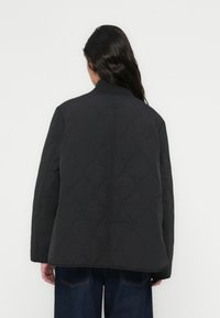 Μαύρο καπιτονέ μπουφάν με στρογγυλή λαιμόκοψη και μακριά μανίκια, με υφή κυματιστού μοτίβου. Η πλάτη είναι απλή και ελαφρώς εφαρμοστή.