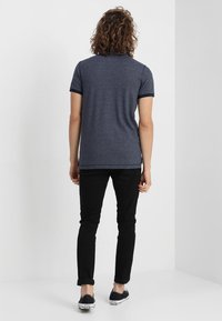 Mörkblå pikétröja med korta ärmar, ribbad krage och kontrasterande manschetter, kombinerad med svarta slim-fit byxor och avslappnade svarta skor.