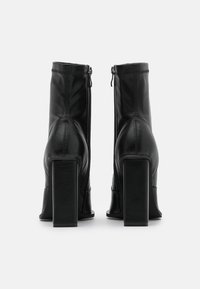 Černé kožené kotníkové boty s vysokými čtvercovými podpatky, zadním zipem a švy. Hladký povrch s elegantním siluetu.