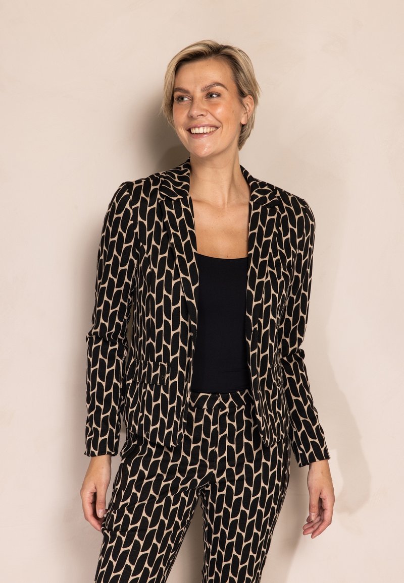 Schwarz-beiges Anzugset mit einem taillierten Blazer mit Reverskragen und schmal zulaufenden Hosen. Strukturierter Stoff mit geometrischem Muster.