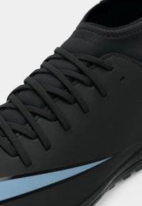 Zapatilla deportiva negra con una superficie lisa, que presenta cordones negros, una franja de acento azul claro y una suela texturizada.