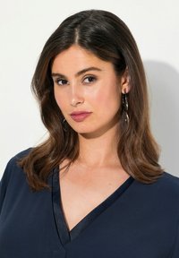Top blu navy con scollatura a V e rifiniture in satin. La modella ha i capelli castani di lunghezza media e indossa orecchini a cerchio argentati. Sfondo neutro.