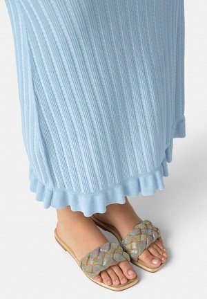 Pies con sandalias planas tejidas multicolores combinadas con una falda azul claro acanalada con un dobladillo fruncido.