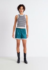White and black striped sleeveless top paired with teal satin shorts featuring a lace trim. Model wearing black cowboy boots.