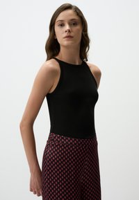 Zwarte geribbelde tanktop gecombineerd met hoogzittende gestreepte broek met rode diamanten op een donkere achtergrond. Gladde stoftextuur.