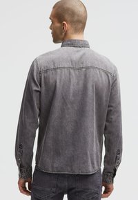 Graue Denimjacke mit klassischem Kragen, langen Ärmeln, geknöpften Manschetten und einer verblassten Textur. Nähte entlang der Säume.