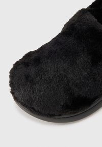 Scarpa nera slip-on con tomaia in morbida ecopelliccia testurizzata e suola liscia e piatta. Forma arrotondata senza hardware o decorazioni visibili.
