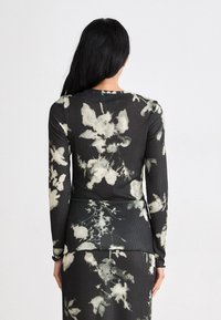 Schwarzes Langarmshirt mit floralem Design in cremefarbenen Tönen. Strukturierter Stoff mit figurbetonter Form und Rundhalsausschnitt, ausgestattet mit gerippten Details.
