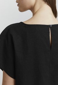 Top in lino nero con scollo a barca ampio, maniche corte e piccolo bottone sul retro con apertura a occhio di pernice.