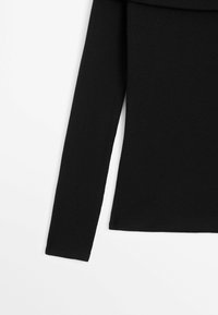 Top lungo nero a maniche lunghe realizzato in tessuto a costine. Caratterizzato da un design aderente e un orlo dritto senza decorazioni.