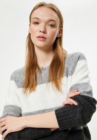 Gestreifter Strickpullover in Weiß, Hellgrau und Dunkelgrau. Mit Rundhalsausschnitt und gerippten Bündchen. Weiche Textur.