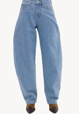 Jean en denim bleu clair taille haute avec des ornements multicolores en strass, porté avec des bottes pointues marron foncé.