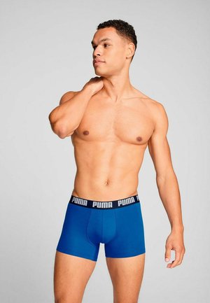 Blaue Boxer-Shorts mit schwarzem Bund und weißem "PUMA"-Branding. Glatte Textur, figurbetontes Design und mittellange Beinlänge.