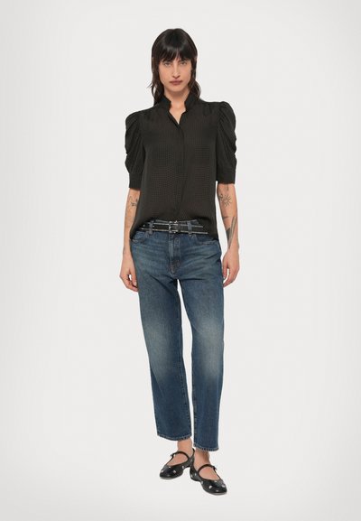 Czarna bluzka w kratę z bufkami, zestawiona z niebieskimi jeansami o prostych nogawkach i czarnymi płaskimi butami, stojąca na białym tle.