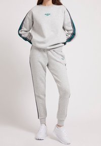 Conjunto de sudadera y pantalones jogger en gris claro, confeccionado en una tela suave, con franjas laterales en teal y marino, además de un pequeño logo en el pecho y en el muslo.