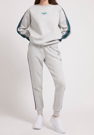 Ensemble de sweat-shirt et de joggers gris clair en tissu doux, avec des bandes latérales teal et marine et un petit logo sur la poitrine et la cuisse.