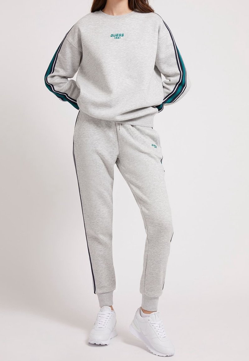 Conjunto de sudadera y pantalones jogger en gris claro, confeccionado en una tela suave, con franjas laterales en teal y marino, además de un pequeño logo en el pecho y en el muslo.