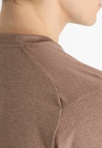 Brown textured shirt featuring a grid pattern, with a round neckline and a smooth fabric finish. Shows shoulder seam detail.