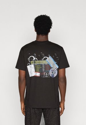 Camiseta de algodón negra que presenta un gráfico de señales de salida de aeropuerto y tarjetas de embarque, con detalles coloridos y acentos de burbujas en la parte posterior.