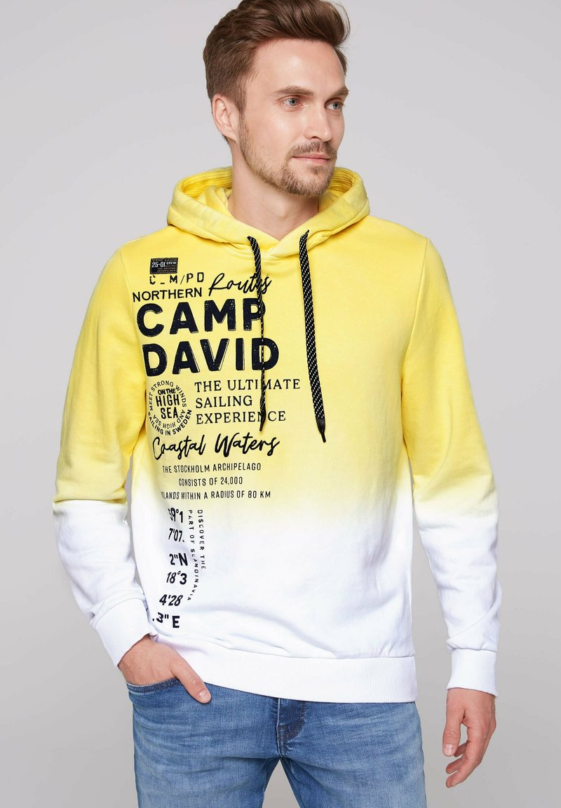 Sudadera con capucha en degradado amarillo y blanco con cordones negros, que presenta texto y gráficos impresos en la parte frontal. Material de algodón, ajuste casual.