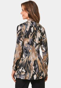 Langwerpig shirt in zwart, met een levendig, abstract patroon van beige en grijze penseelstreken, met een uitlopende zoom en een gladde textuur.