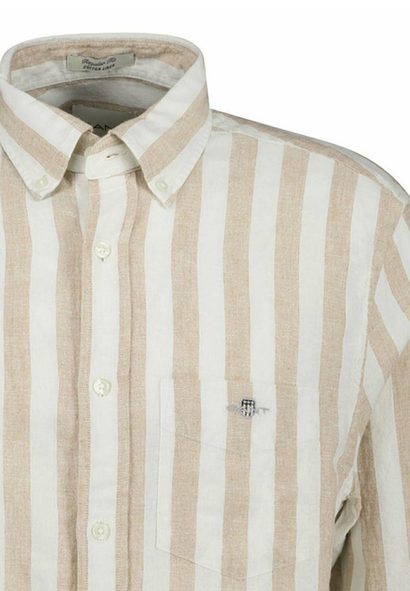 Camicia a righe con colori crema chiaro e beige, colletto con bottoni, tasca frontale con logo e tessuto morbido e testurizzato.
