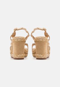 Sandali wedge in suede beige con finitura in juta intrecciata, apertura posteriore e cinturini alla caviglia regolabili. Presentano una superficie liscia e una suola solida.
