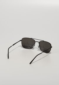 Ochelari de soare de tip black metal, cu lentile întunecate rectangulare, brațe subțiri și tampoane de nas clare. Design simplu, fără modele decorative.