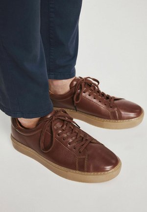 Brązowe skórzane trampki o teksturowanym wykończeniu, okrągłym nosku i gumowej podeszwie. Posiadają sznurowaną konstrukcję i kontrastującą beżową podeszwę.