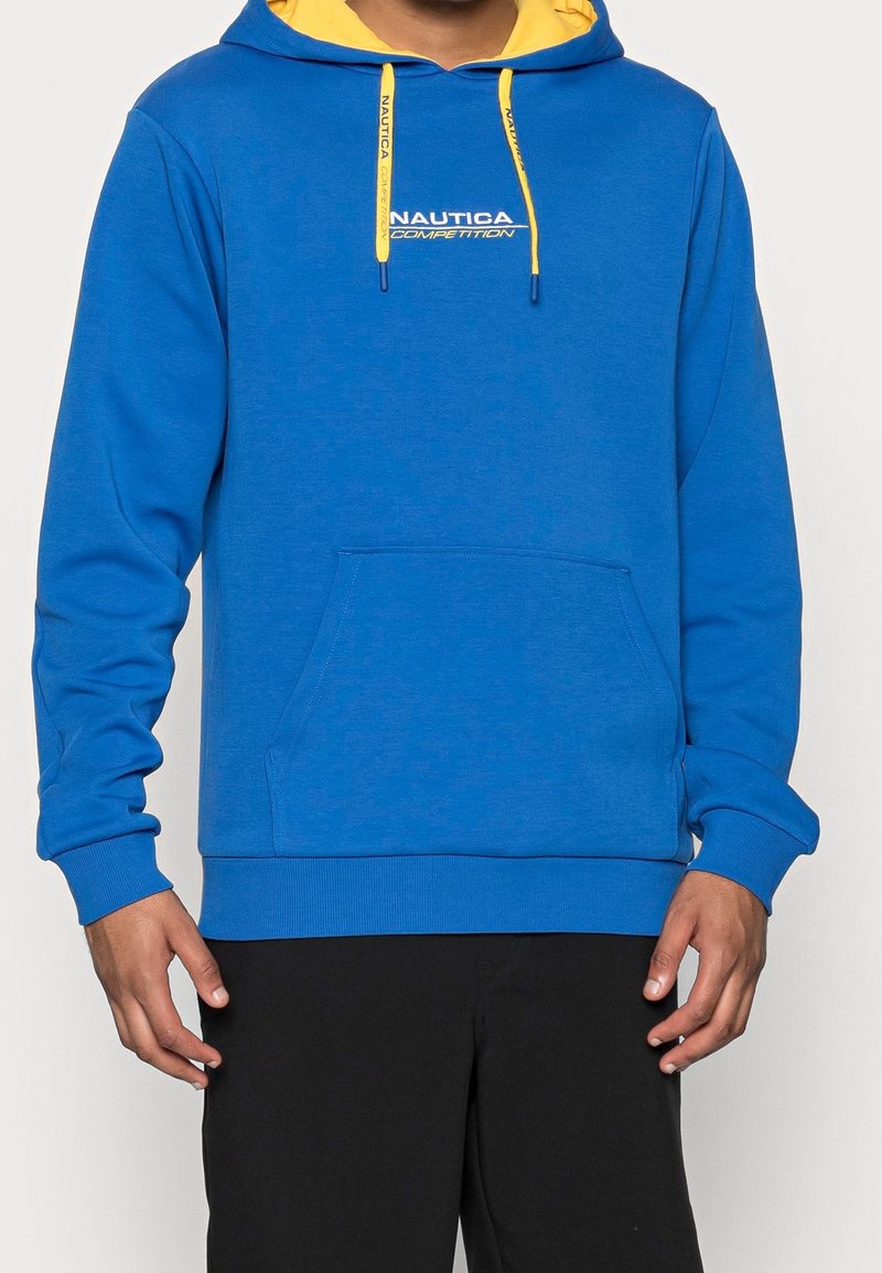 Blå huvtröja med ett gult foder, med en framficka och en grafisk logo. Materialet är mjukt och slätt.