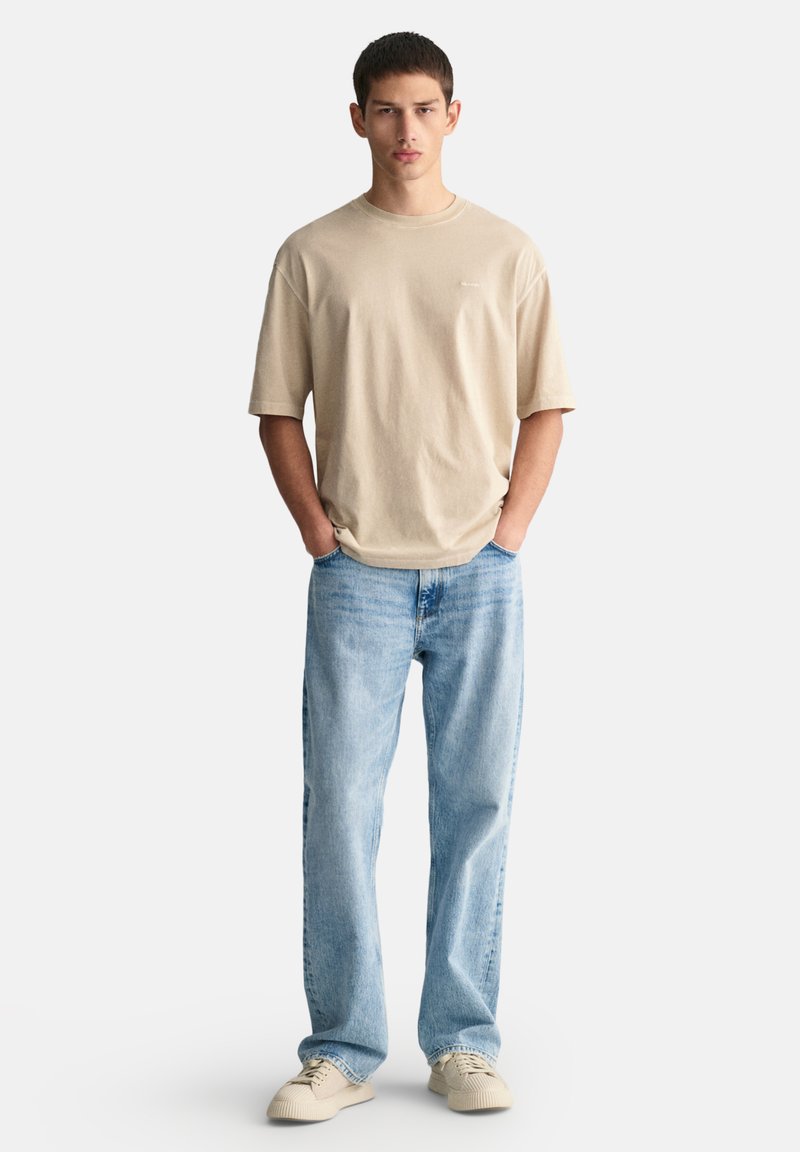 Camiseta de manga corta beige con un corte relajado, combinada con jeans rectos de color azul claro y zapatillas beige. Diseño sencillo y limpio.