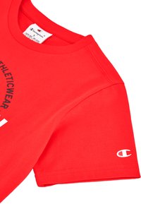 Camiseta de algodón roja con cuello redondo y mangas cortas. Presenta el texto negro "Athletic Wear" y un logo blanco en la manga.