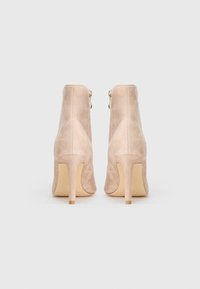 Bottes de cheville en suede nude avec une silhouette élégante, de hauts talons aiguilles et une fermeture éclair à l'arrière. Texture lisse avec un minimum de détails.