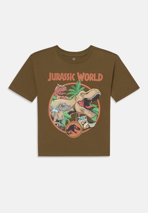 Braunes Baumwoll-T-Shirt mit einem "Jurassic World"-Grafikdesign, das Dinosaurier und Palmenblätter in leuchtenden Farben innerhalb eines kreisförmigen Designs zeigt. Kurze Ärmel.